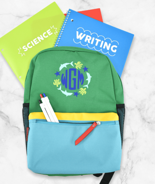 A boys backpack with a color block design, and green and blue notebooks, all with customized smart vinyl decals applied to the fronts.
