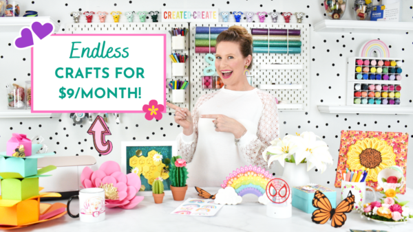 Abbi Kirsten stands behind a desk in her craft room surrounded by colorful supplies. She is pointing to an inset text box that says "Endless crafts for $9/month." Join the Abbi Kirsten Collections premium member vault and gain access to unlimited SVG files, templates, tutorials and more.