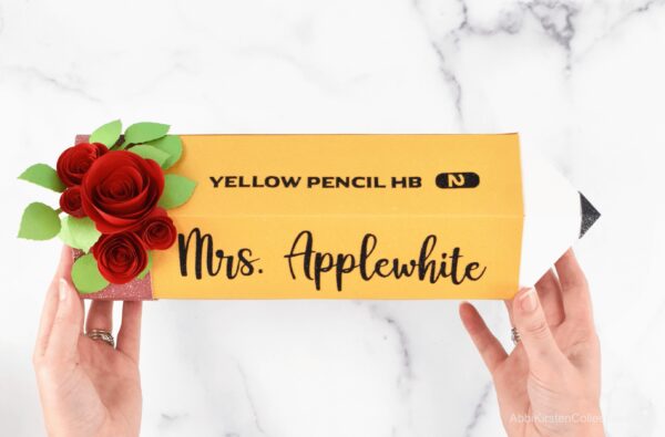 Abbi's hands hold a large paper pencil. red roses and green leaves decorate one end of the pencil. Black vinyl words say "yellow pencil number 2" and "Mrs. Applewhite."