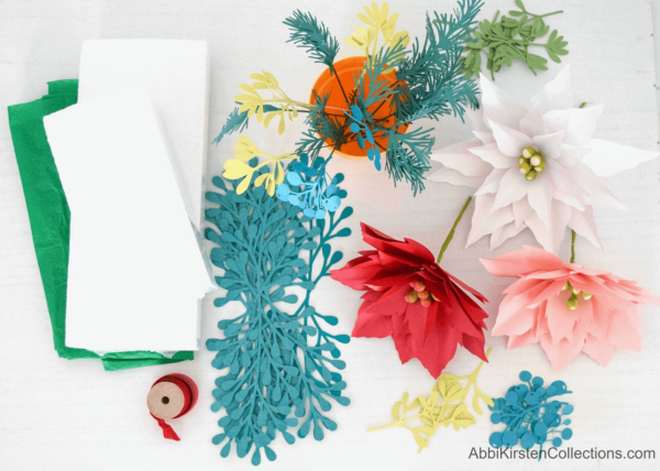 Supplies needed to make paper poinsettia flowers, laid out on a white crafting table.