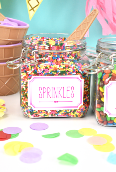 Cricut Joy Smart Vinyl Labels on jars of sprinkles and other candies. Colorful confetti circles lay in front of the jars. 