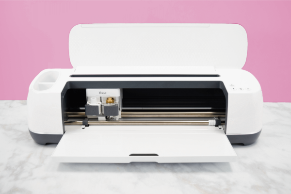 Cricut Maker machine on a white desk with a pink background