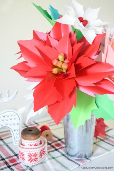 A large stemmed red paper poinsettia flower in a metal vase, on a Christmas tablescape.