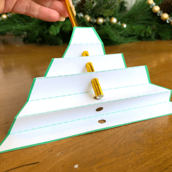 The gold paper straw is inserted into each folded section through the punched holes to create the body of the Christmas angel. This is an easy craft for kids!
