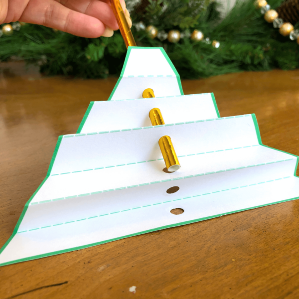 A paper cut-out in the shape of a tree is folded accordion-style, with a silver paper straw inserted through the center.