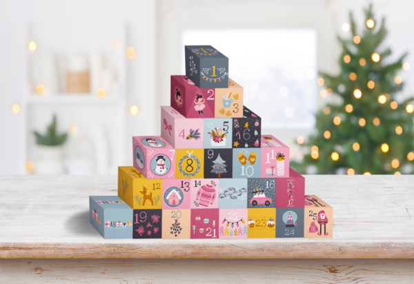 A sparkling Christmas tree is the background for a completed pyramid of DIY advent calendar boxes. Download the free printables for your holiday!