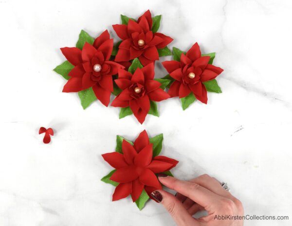 Abbi Kirsten's hand adds the medium-sized petals to the paper poinsettia for the Christmas Wreath. Finished paper flowers adorn the table.