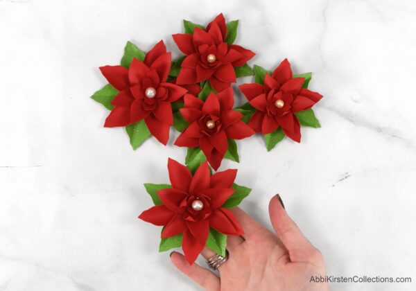 Abbi Kirsten has one paper poinsettia flower in her hand while another four paper flowers are nearby, ready to be added to the DIY Christmas wreath.