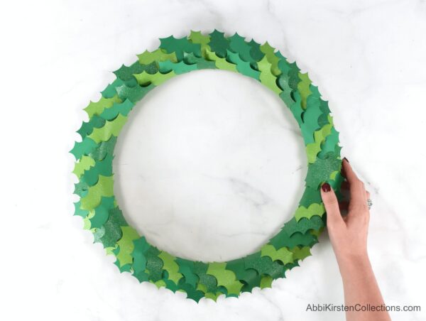 Abbi Kirsten holds a Christmas wreath after she covered the entire wreath with paper holly leaves.