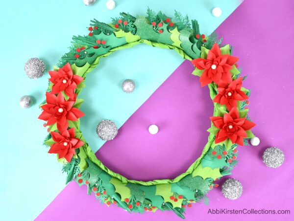 DIY Christmas wreath with poinsettia paper flowers and holly. Use your Cricut machine to make a custom DIY holiday wreath out of paper. 