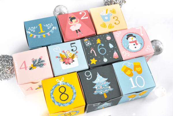 Ten printable advent calendar boxes stacked on a table next to each other. These personalized Christmas boxes can contain small gifts or treats. 