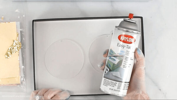 Abbi holds a can of Krylon easy tack adhesive spray to coat to clear acrylic disk ornaments. 