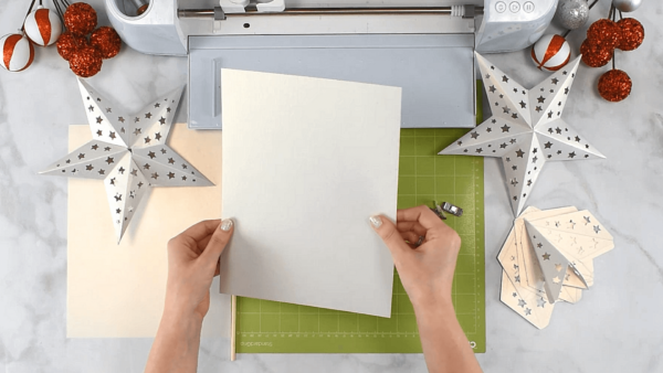 Abbi holds a piece of white cardstock near a Cricut machine. Two paper stars lay near by. 
