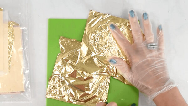 Wearing clear vinyl gloves, Abbi applies sheets of gold leaf paper to the acrylic disk ornaments.