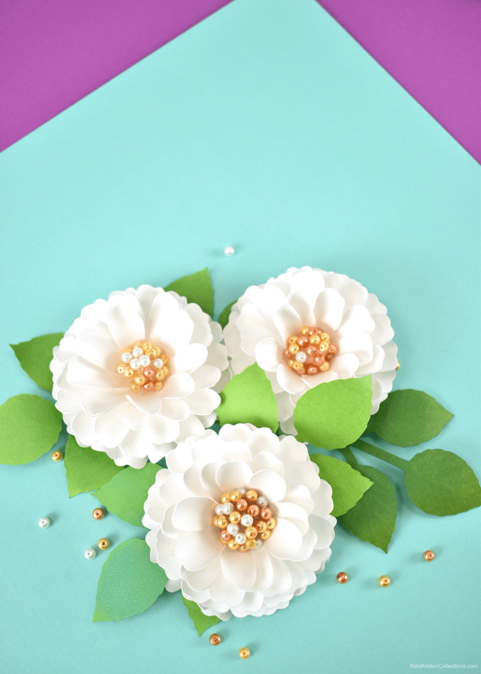 Three small white paper dahlia flowers with pearl centers. Each flower has small green leaves.