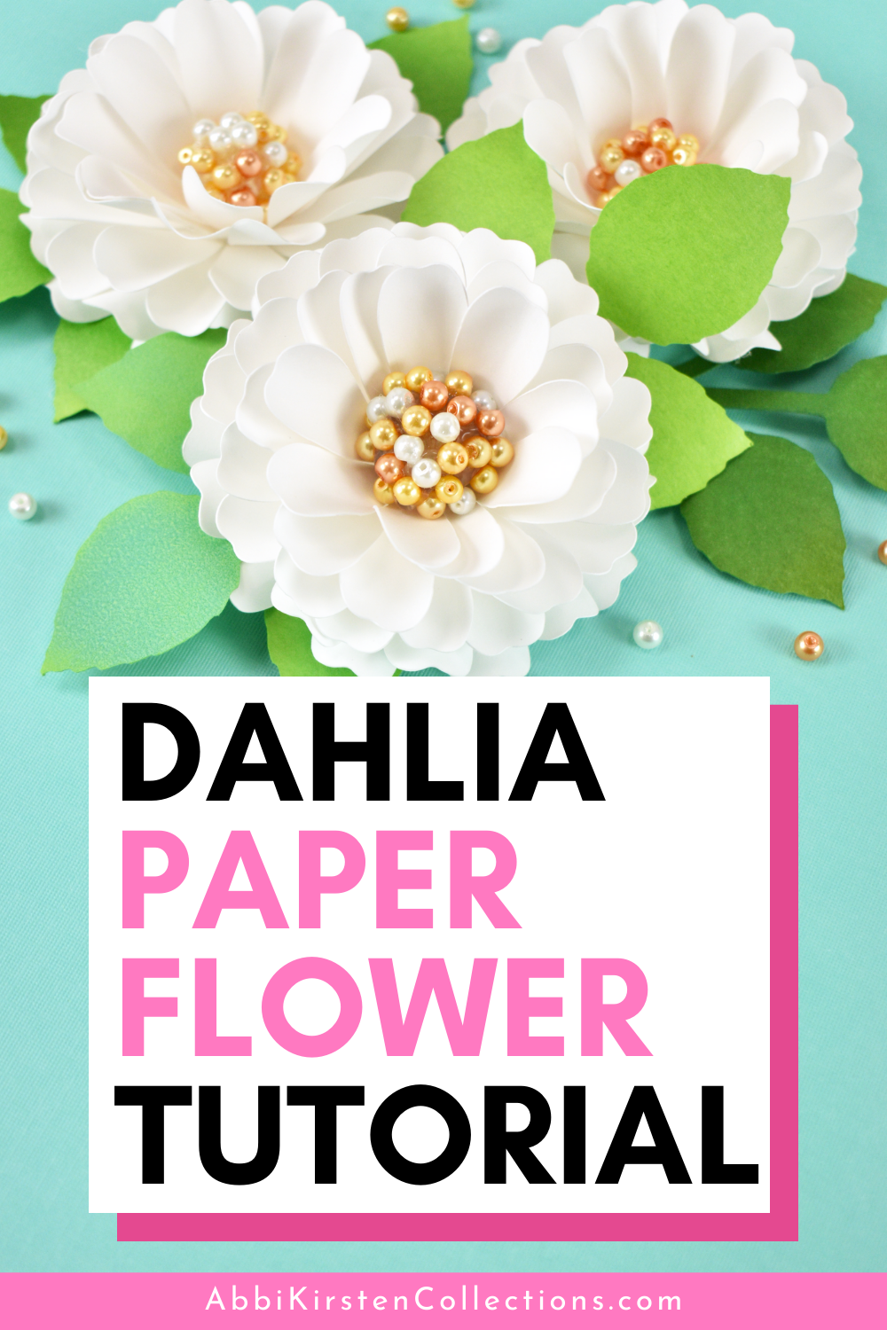 Three white paper dahlia flowers with gold and white pearl centers and green leaves sit on a teal blue background. Text on the image says "dahlia paper flower tutorial"