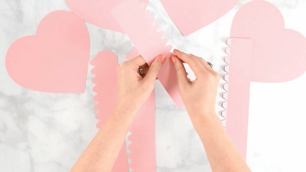 Pink paper heart box templates being folded on top of a marble workstation.  