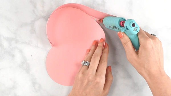 Hot glue being applied to the edges of a pink paper heart. 