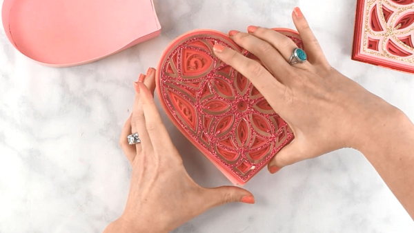 A glittery pink paper heart mandala being applied to the top of the box. 