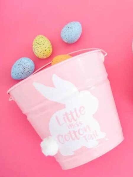 A pink metal Easter bucket with a white vinyl bunny sticker and colorful Easter eggs.