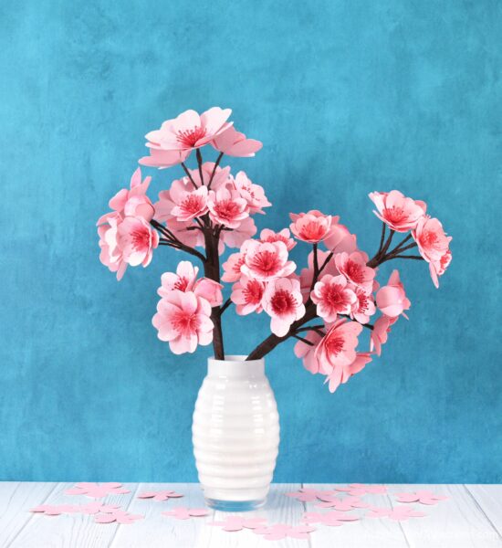 Paper cherry blossoms on a white vase against a blue background.