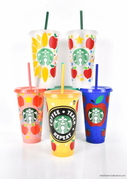 A set of five reusable plastic Starbucks cups decorated with vinyl stickers of apples, flowers, and words for Teacher Appreciation