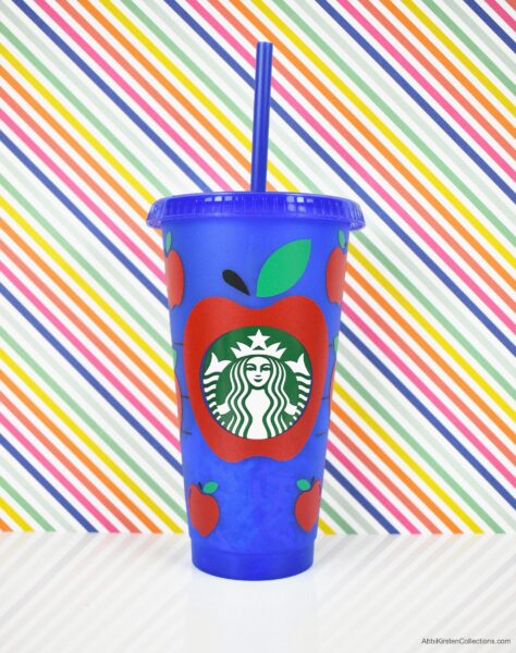 A blue plastic reusable Starbucks cup with an apple vinyl decal. A large apple surrounds the Starbucks logo, with smaller red apples around it. 