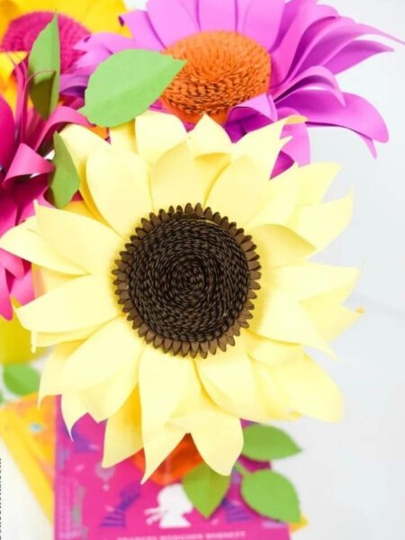 A yellow paper sun flower arranged together with other sunflowers in different colors.