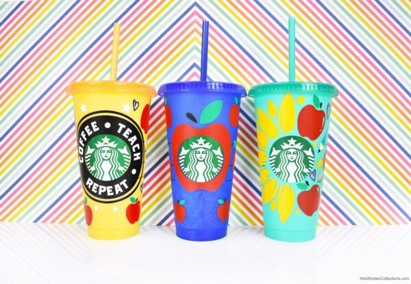 Three reusable plastic Starbucks cups decorated with Teacher Appreciation vinyl decals, up against a rainbow stripped background. The decals contain apples, flowers, words, and hearts for teacher appreciation.