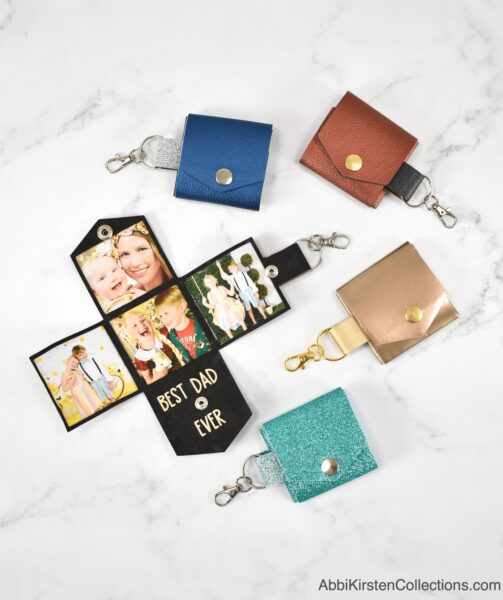 Five photo keychains in the colors black, blue, bronze, gold and turquoise laying on a marble countertop.