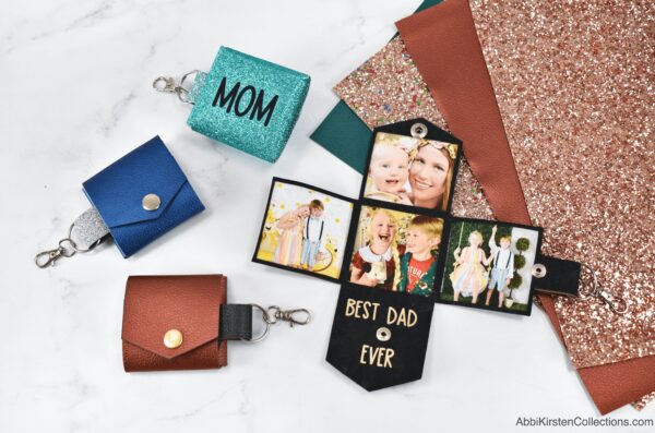 Four DIY faux leather photo keychains in colors turquoise, blue, bronze and black laying on a marble workstation. 