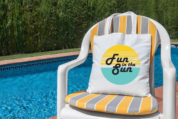 A white plastic chair with gray and yellow cushions is next to an azure-blue pool. A tote bag that reads "Fun in the Sun" sits on the chair.