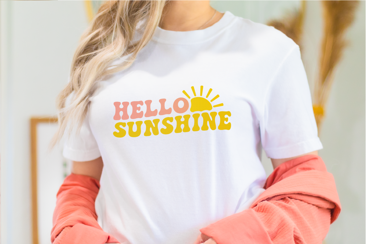 A close-up of a woman wearing a white t-shirt with yellow and pink words that say, "Hello Sunshine." A sun peeks out from the words for extra fun.