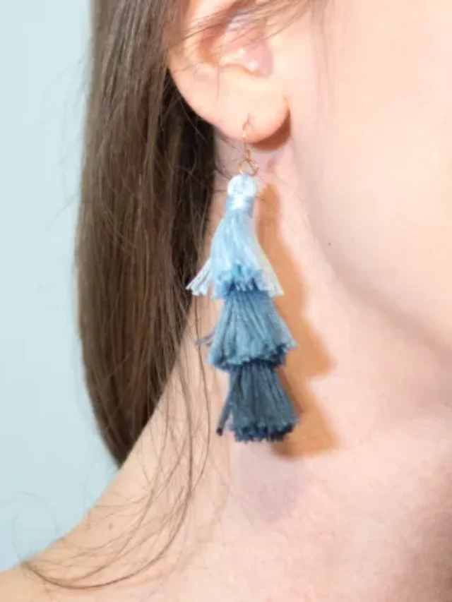 A woman with long hair wearing an ombre tassle earring while smiling