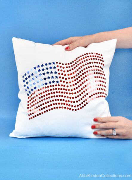 Abbi's hand holds the bottom corner of an American flag with holographic sparkle iron-on vinyl on a pillow case. 