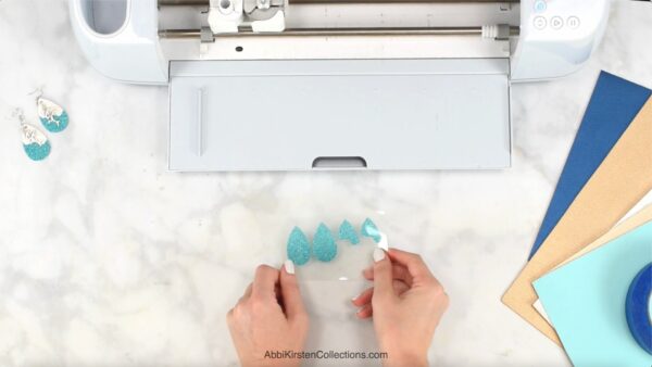 Turquoise faux leather pieces cut in teardrop shapes next to a white Cricut machine.
