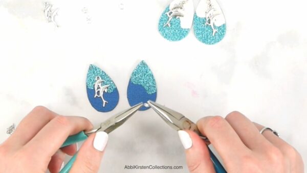 Two pliers adding silver hardware to a set of turquoise and blue faux leather earrings. 