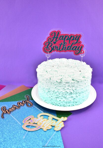 A light blue frosted layer cake with a glittery red and blue sign on top that reads "happy birthday". 