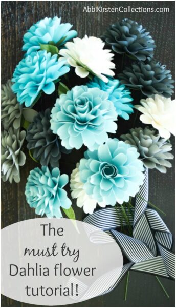A photo of white and light-blue small paper dahlia flowers in a vase with black and white striped ribbon. Image text overlay reads, “the must try dahlia flower tutorial!”