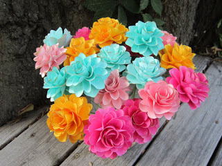 A bouquet of bright blue, orange, and pink small paper dahlia flowers in a vase on a wooden table.