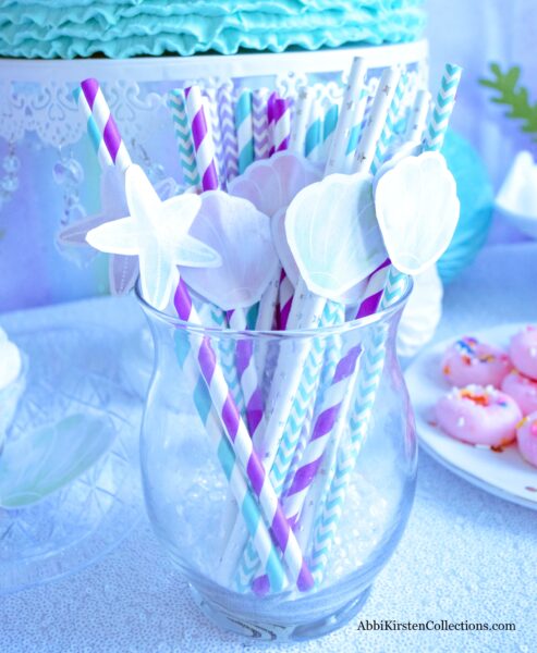 Blue and purple paper straws with starfish and sea shell printables sit in a glass jar on a dessert table.