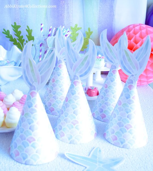 Customized mermaid tail party hats from Print Press Party on Etsy sit on a party table.