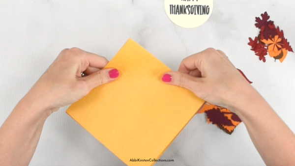 Hands folding a yellow piece of paper with fall leaves on the table. 