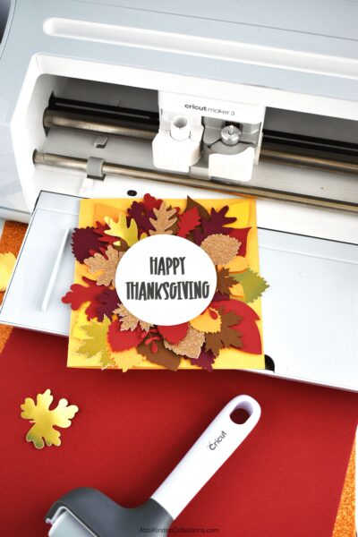 A Happy Thanksgiving card with fall leaves sitting on a Cricut machine with a Cricut tool nearby. 