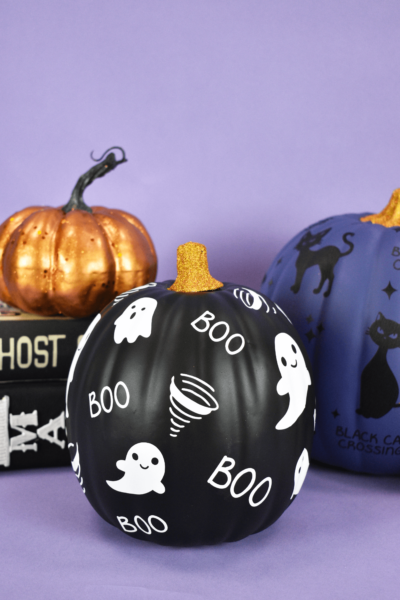 A painted black Halloween pumpkin is covered with Cricut vinyl Halloween designs - little ghosts and the word "boo" in white vinyl.