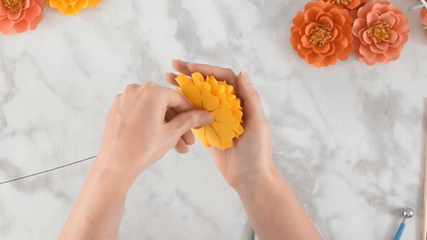 Adding stems to a yellow paper marigold flower. 