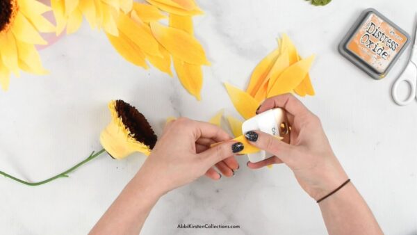 Yellow crepe paper petals are being curled with a Cricut scraper tool by Abbi Kirsten. 