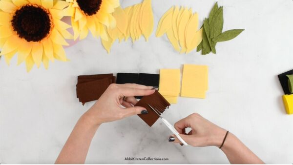 Above crepe paper sunflowers and the separate cut-out elements, Abbi Kirsten's hand use detail scissors to cut out the brown sunflower center. 