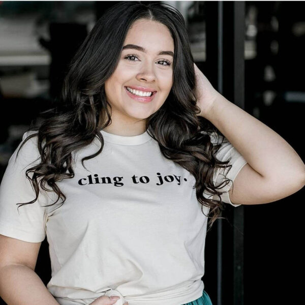A smiling woman models an off-white t-shirt with black text that reads, "Cling to joy." The graphic is a free downloadable encouragement SVG file.