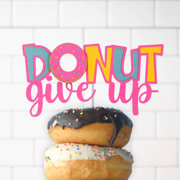 Two frosted donuts with sprinkles are stacked in front of a brick wall.  A cake topper crowning the donuts says, "Donut give up." The colorful cut-out topper is a  funny, free SVG file you can download.
